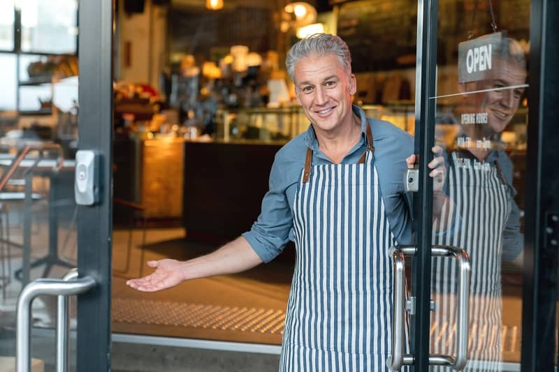 Business owner at the door of a cafe welcoming customers-cm